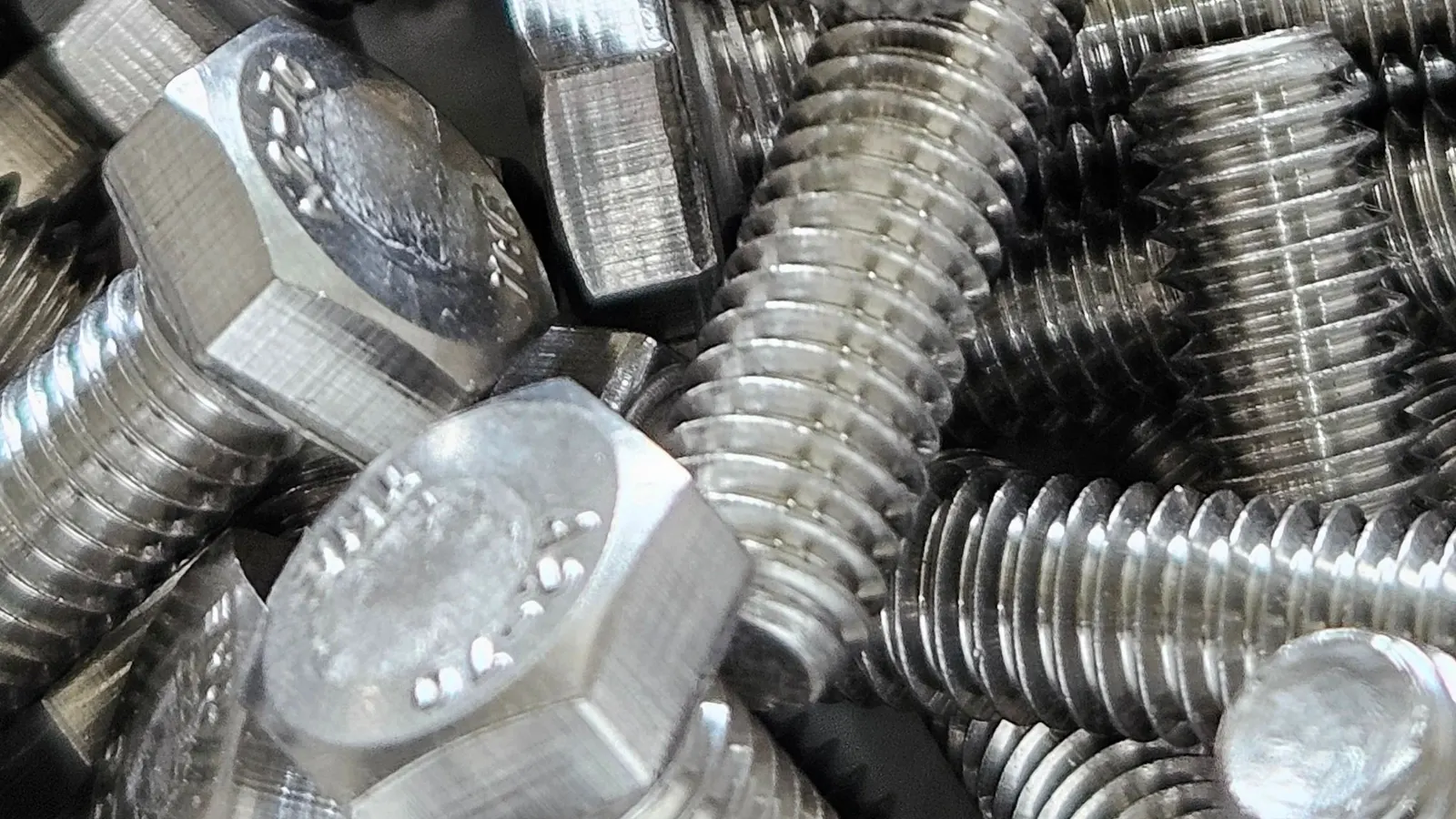 Stainless steel hex head bolts in a pile, plain finish, with grade markings stamped on the heads.
